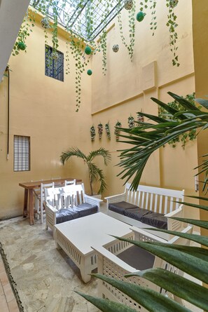 Une cour ensoleillée avec un ensemble de meubles de jardin blancs, une petite table et des plantes en pot.