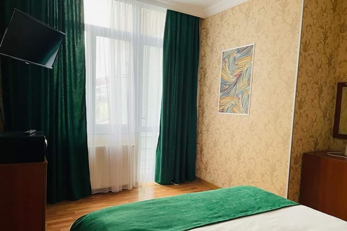 Habitación de hotel con cama, televisor de pantalla plana, ventana con cortinas translúcidas y pared con diseño.