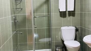 A bathroom with a glass-enclosed shower, a toilet, a sink, and a towel rack with towels.