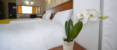A hotel room with a large bed, a bedside table with a potted orchid, and a mirror above the bed.
