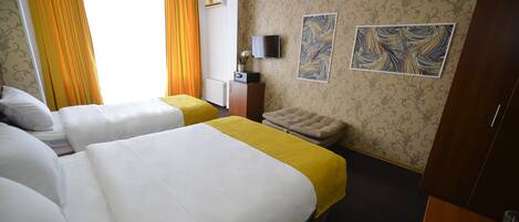 A hotel room with two beds, a sofa, a TV, and artwork on the wall.