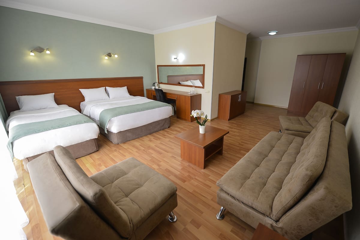 Habitación de hotel con dos camas, un escritorio, una silla, un sofá y un armario.