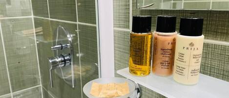A bathroom with a glass shower enclosure, a white sink, and three bottles of shampoo and body cream on the sink.