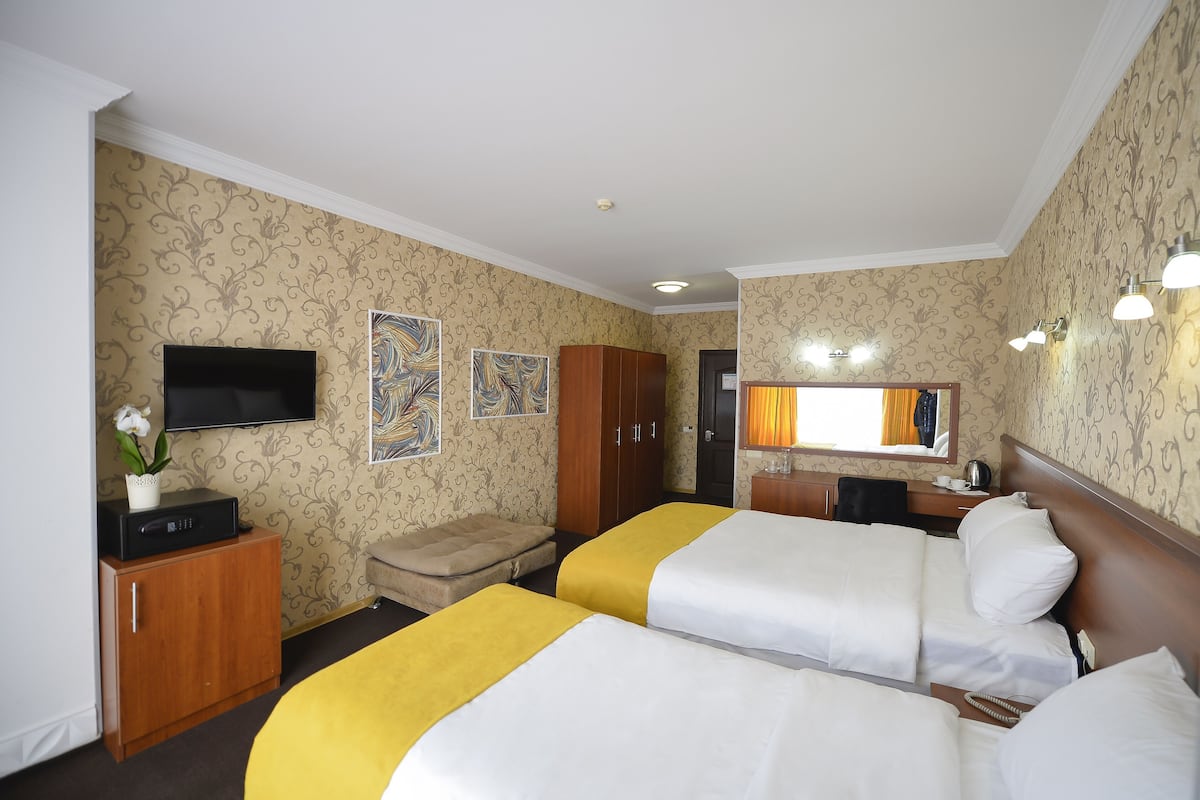 Habitación de hotel con dos camas, televisión, armario, escritorio con lámpara y obras de arte en las paredes.