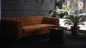 Un sofá color café con tapizado texturizado en una habitación moderna, con una mesa de centro de vidrio y plantas en macetas.