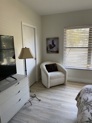 Relax in a serene bedroom with a flat-screen TV, armchair, and large window offering a view.