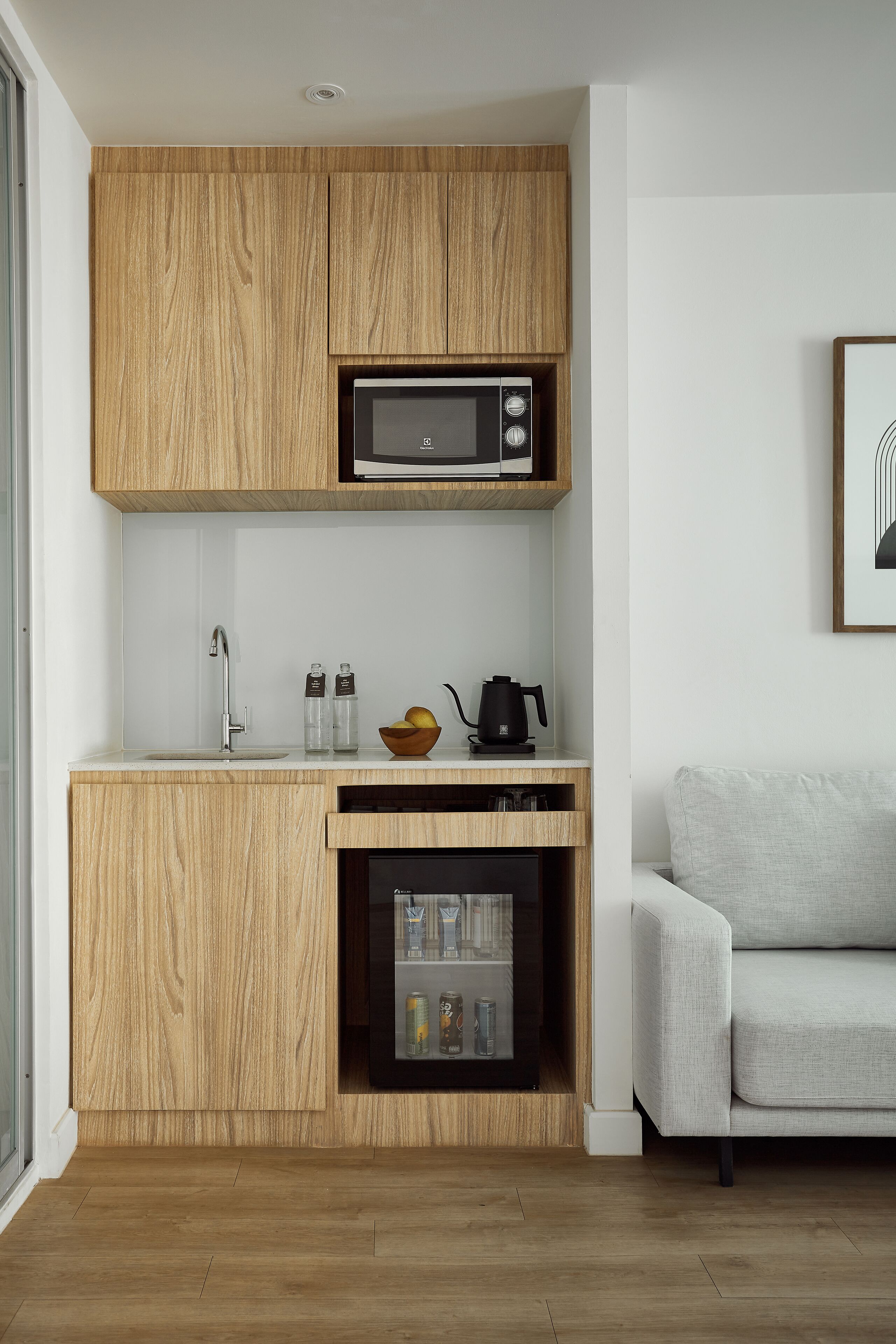 A compact kitchen with wooden cabinetry, a microwave, a kettle, and a small refrigerator.