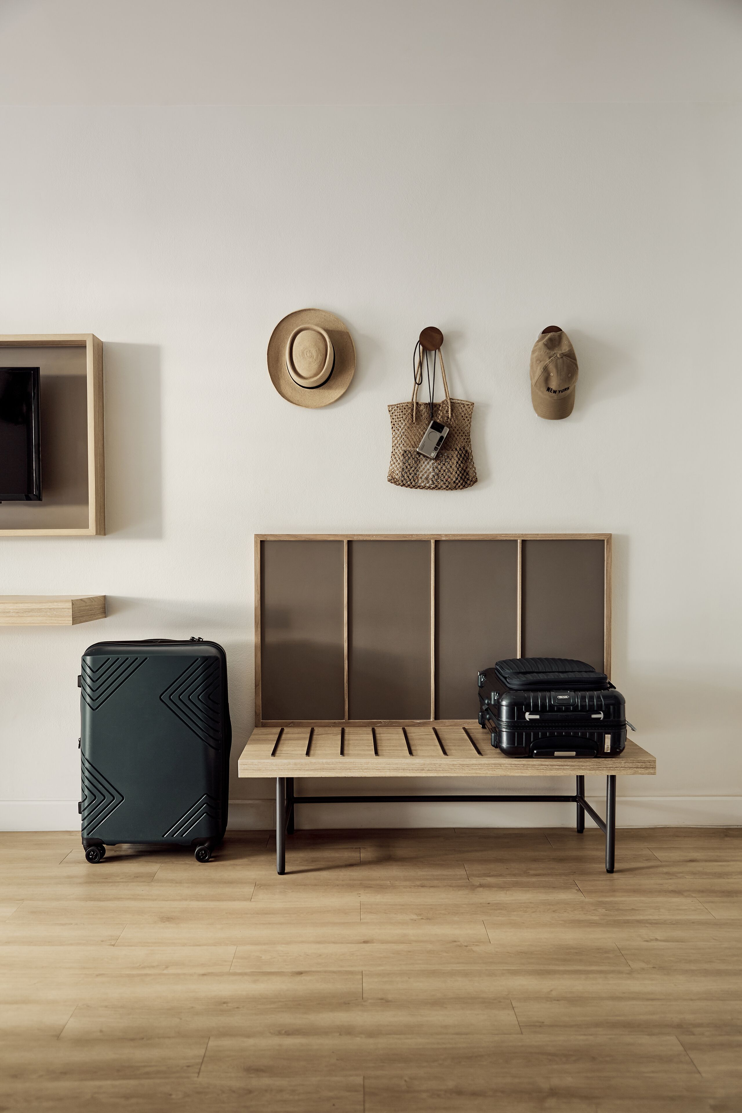 A room with a wooden bench, two suitcases, a hat, and a handbag on the wall.