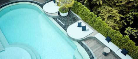 Un área de piscina moderna al aire libre con un diseño curvo, rodeada de setos bien cuidados y plantas en macetas.
