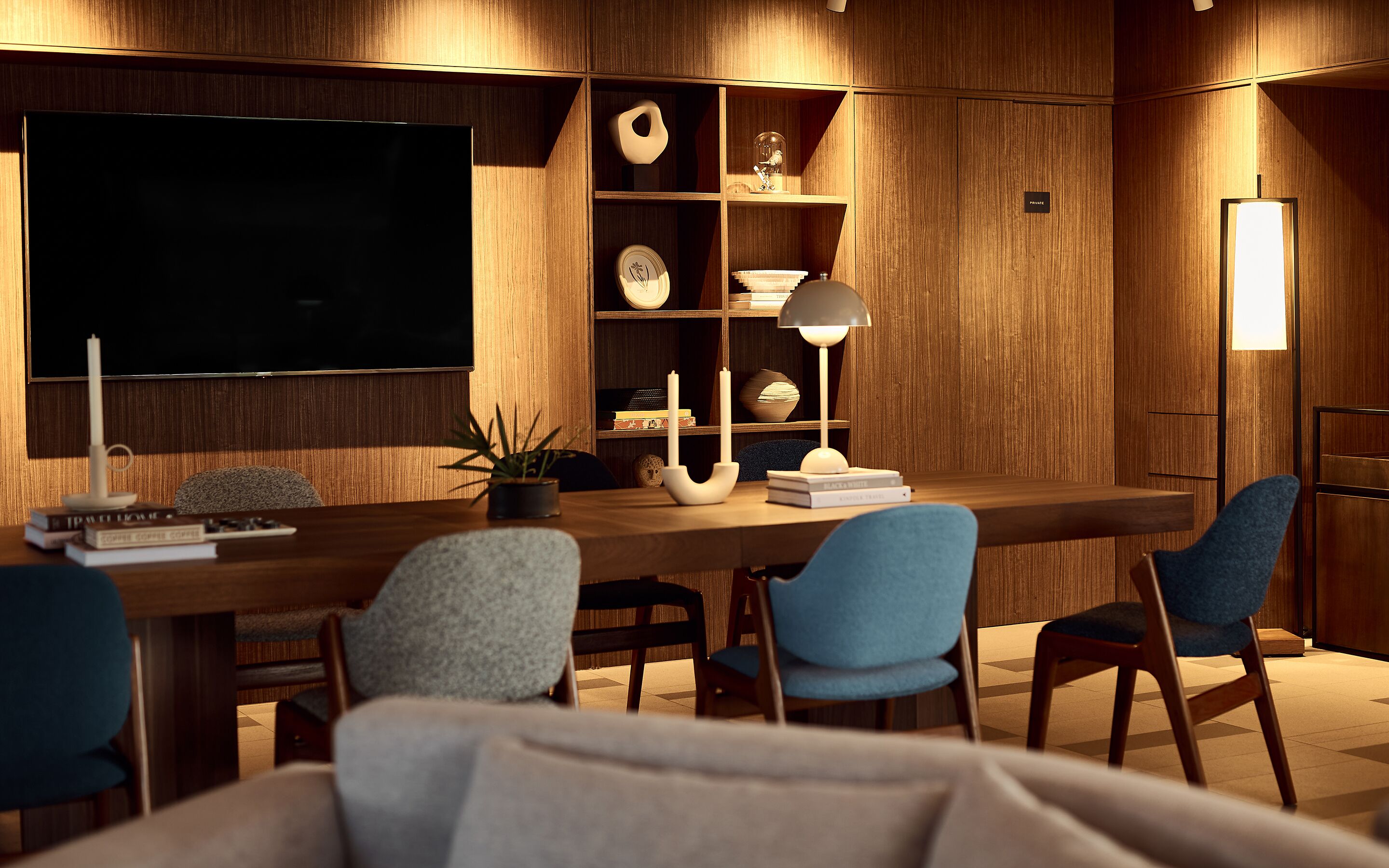 Ein moderner, gut beleuchteter Raum mit einem großen Flachbildfernseher, Holzregalen mit Dekoration und einem Schreibtisch mit Stühlen.
