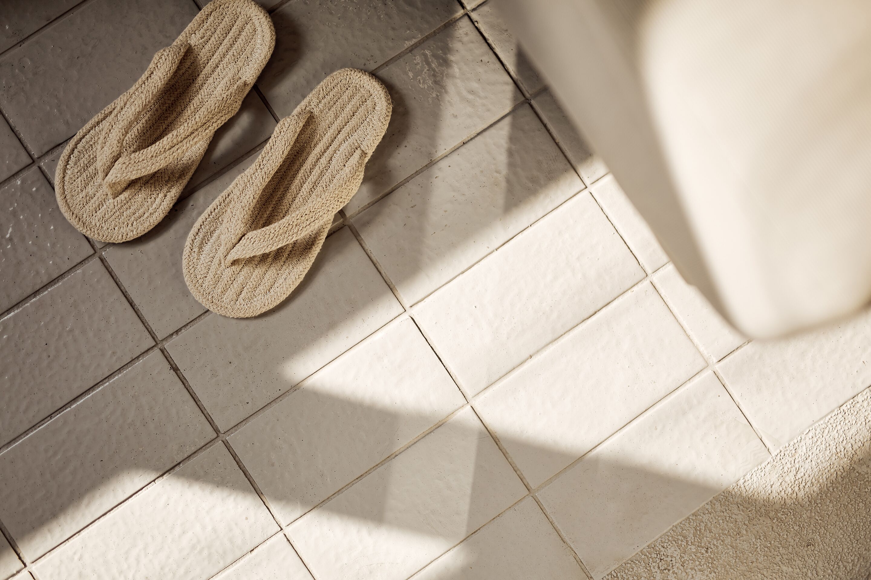 A pair of woven slippers on a tiled floor.