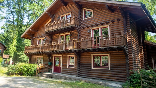 A multi-story log cabin with a balcony on the second floor, a front door, and a small porch. - Les Pins Sylvestres (Amneville)