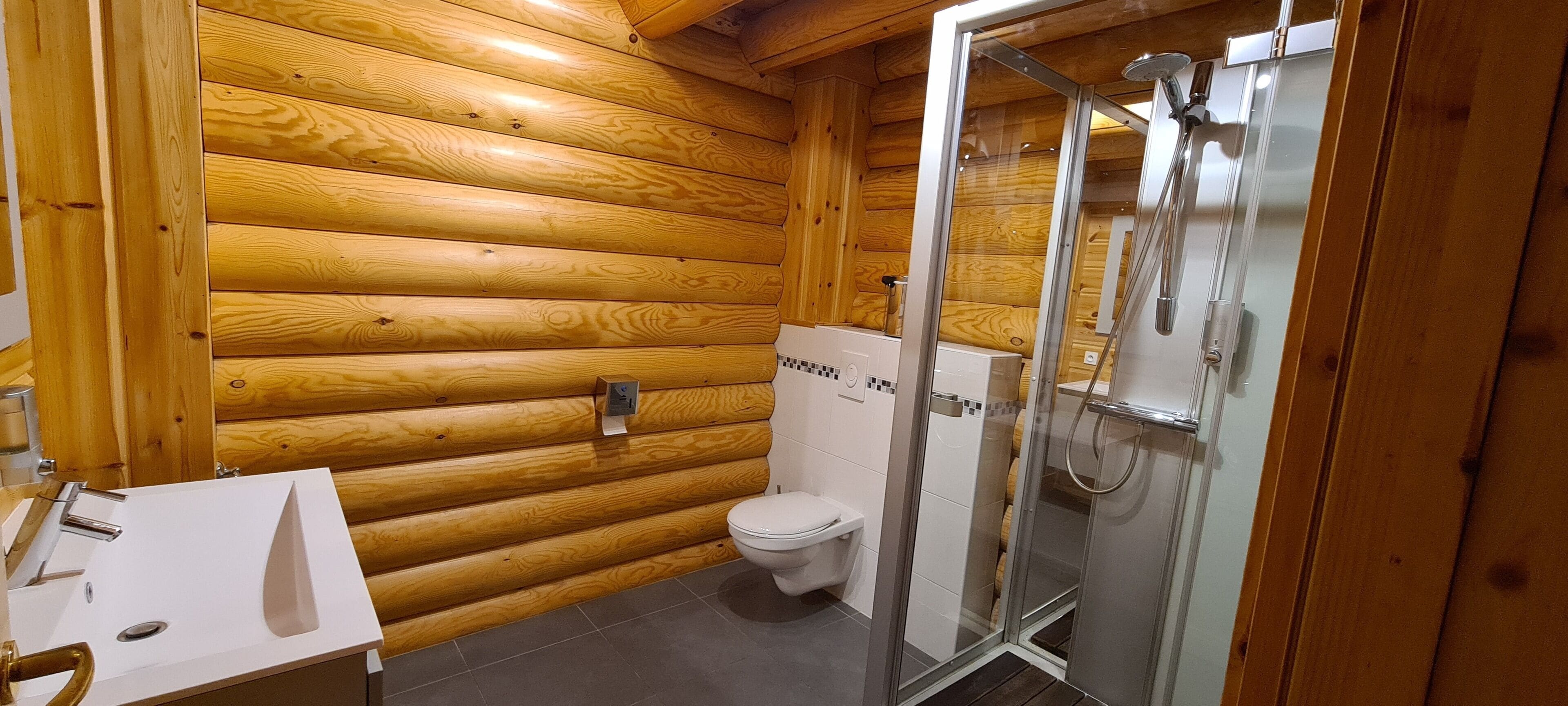 Een houten badkamer met een witte wastafel, toilet en douchecabine met glazen wanden.