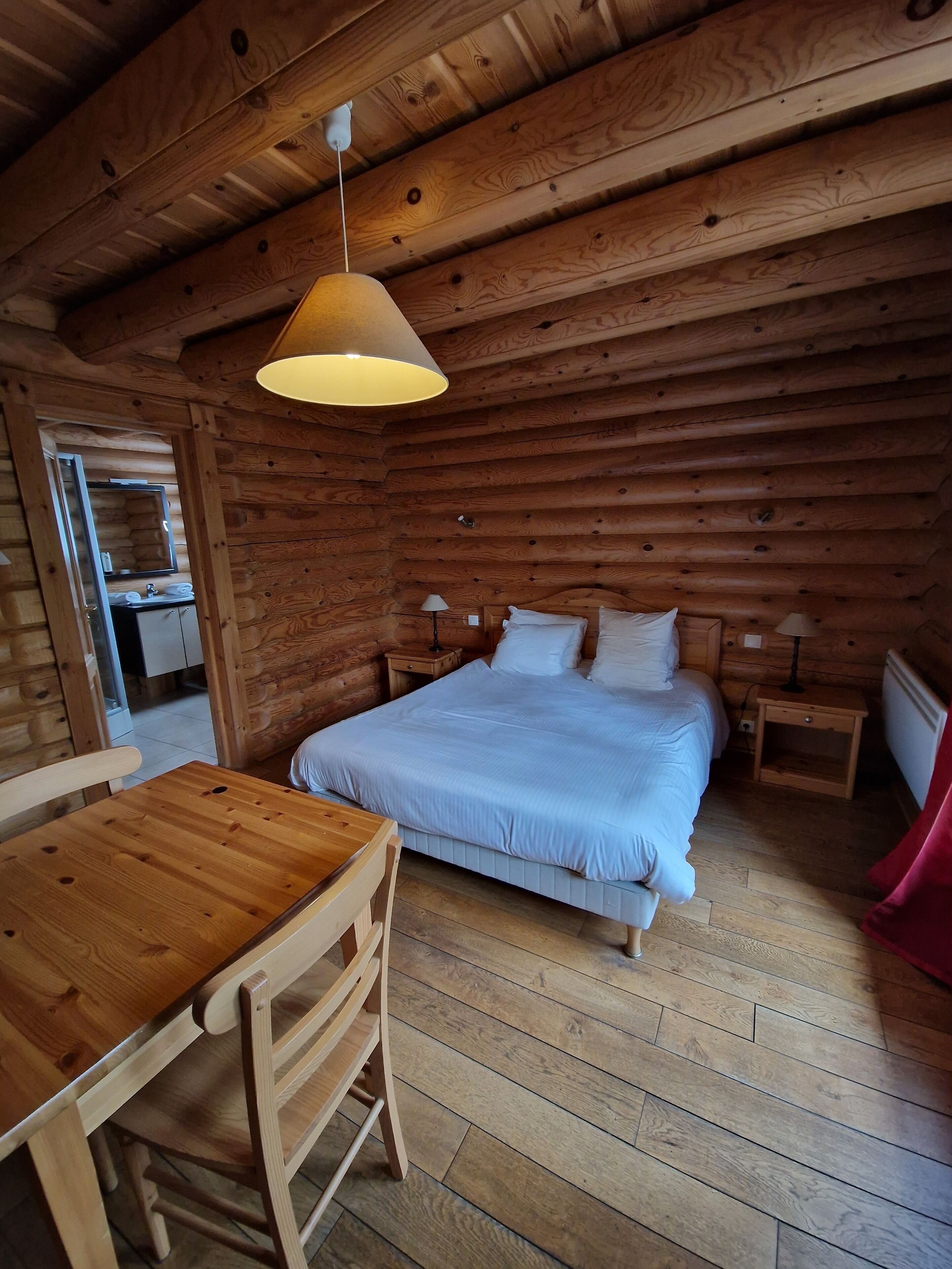 A wooden cabin interior with a bed, a table, and a chair.