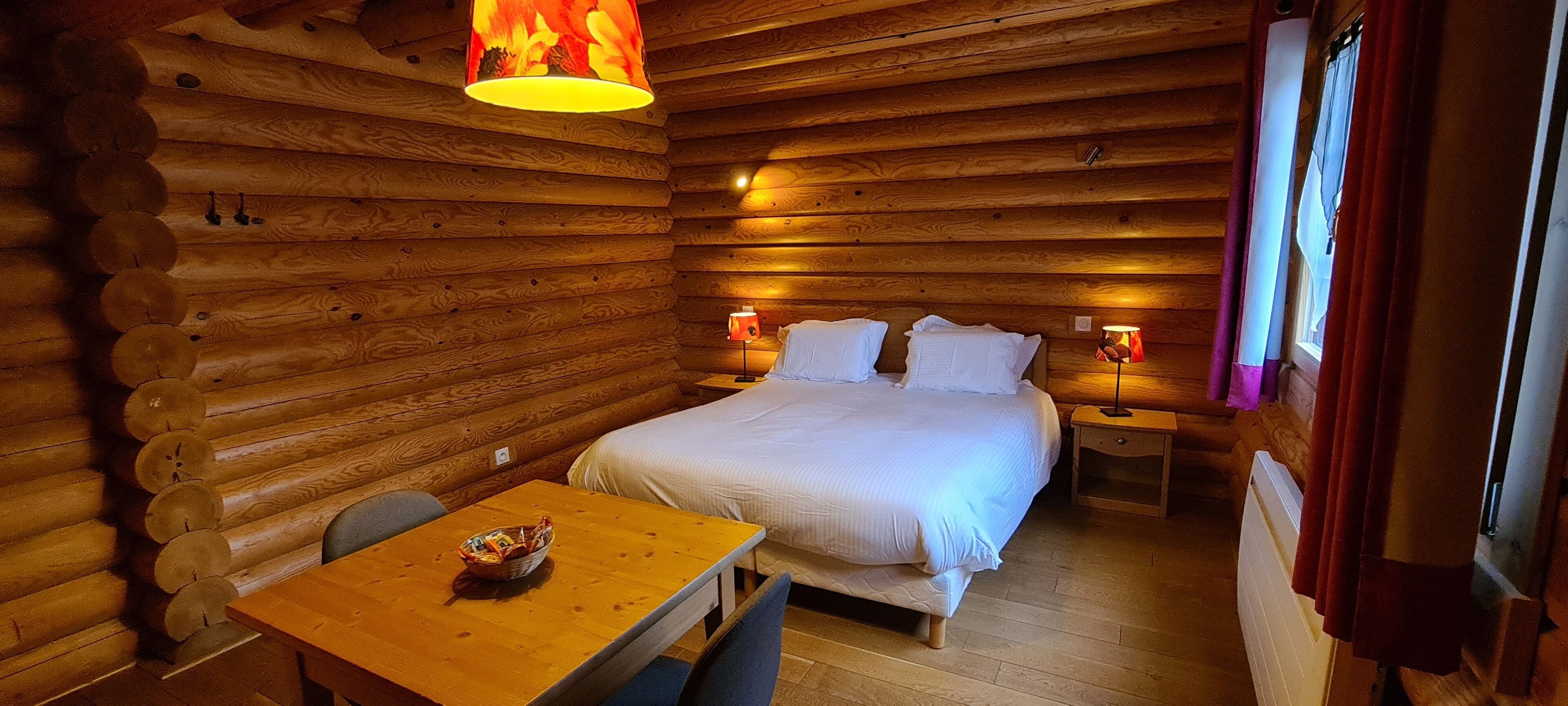 Une chambre rustique aménagée dans un chalet en bois, avec un lit en bois, une table sur laquelle se trouve un panier, et deux lampes de chevet.