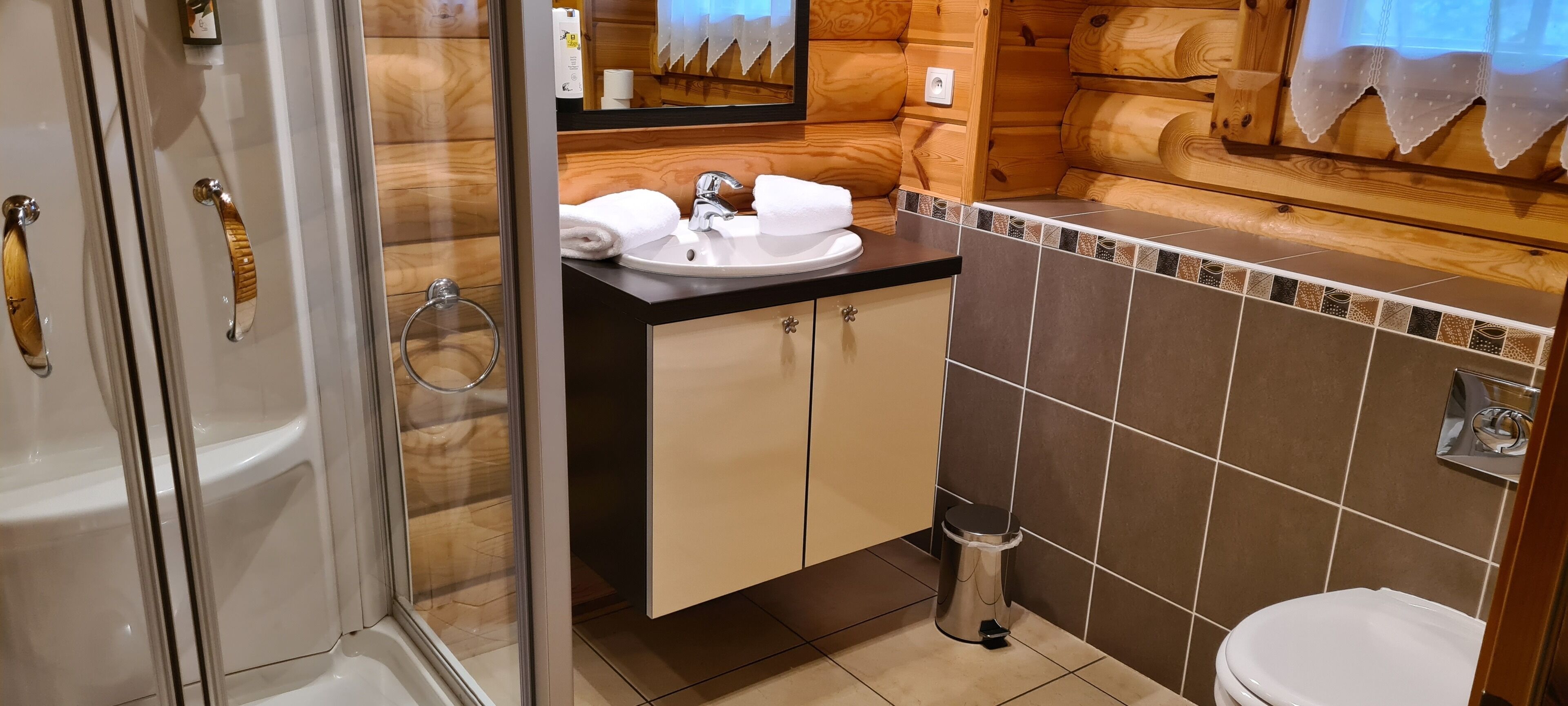 A bathroom with a glass shower enclosure, a sink with two towels, and a toilet.
