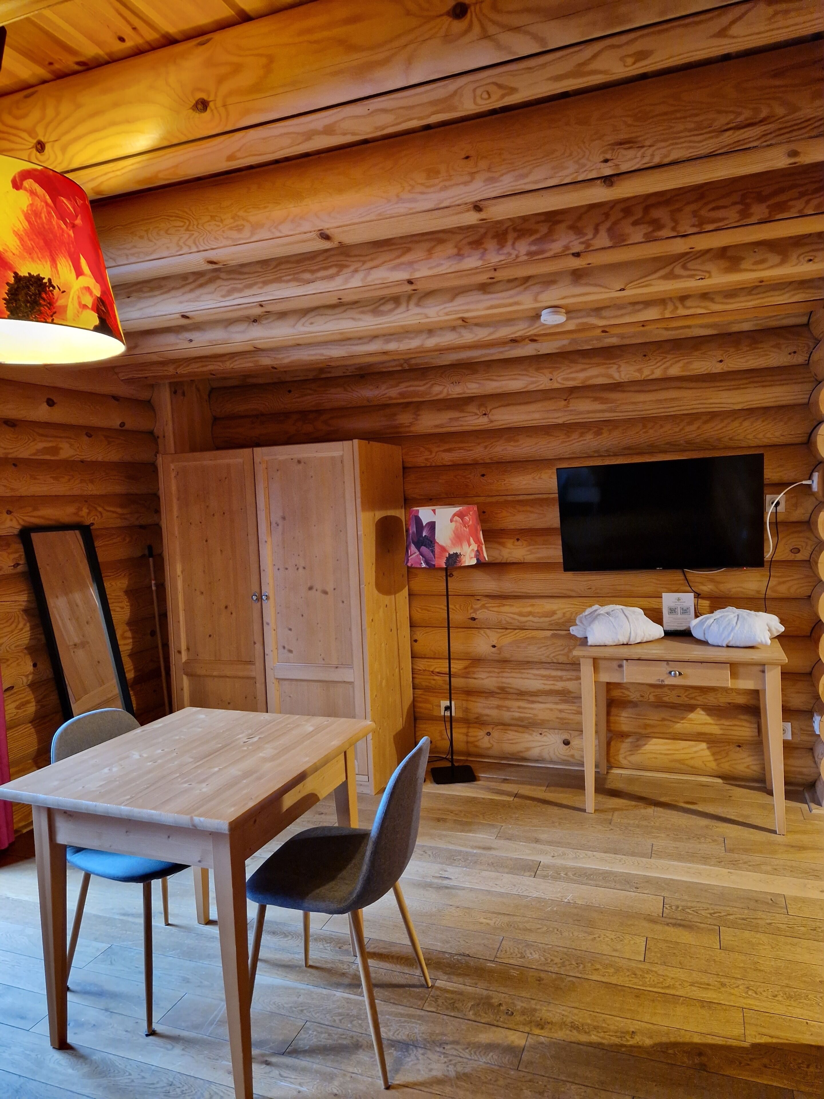 Interior de una cabaña de madera con una mesa de comedor, sillas, un televisor y un armario.
