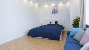 Une chambre avec un lit, un canapé bleu, une plante en pot et une affiche représentant un paysage urbain accrochée au mur.