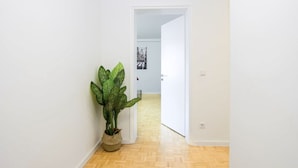 Un couloir avec une plante en pot, un plancher en bois et une porte blanche donnant sur une autre pièce.