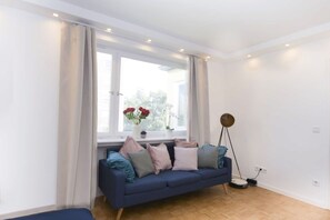 A modern living room with a blue sofa, a small table with a vase of flowers, and a floor lamp.