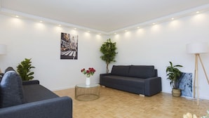 Un salon moderne avec un canapé gris, une table basse ronde ornée d’un vase de fleurs et une grande plante en pot.