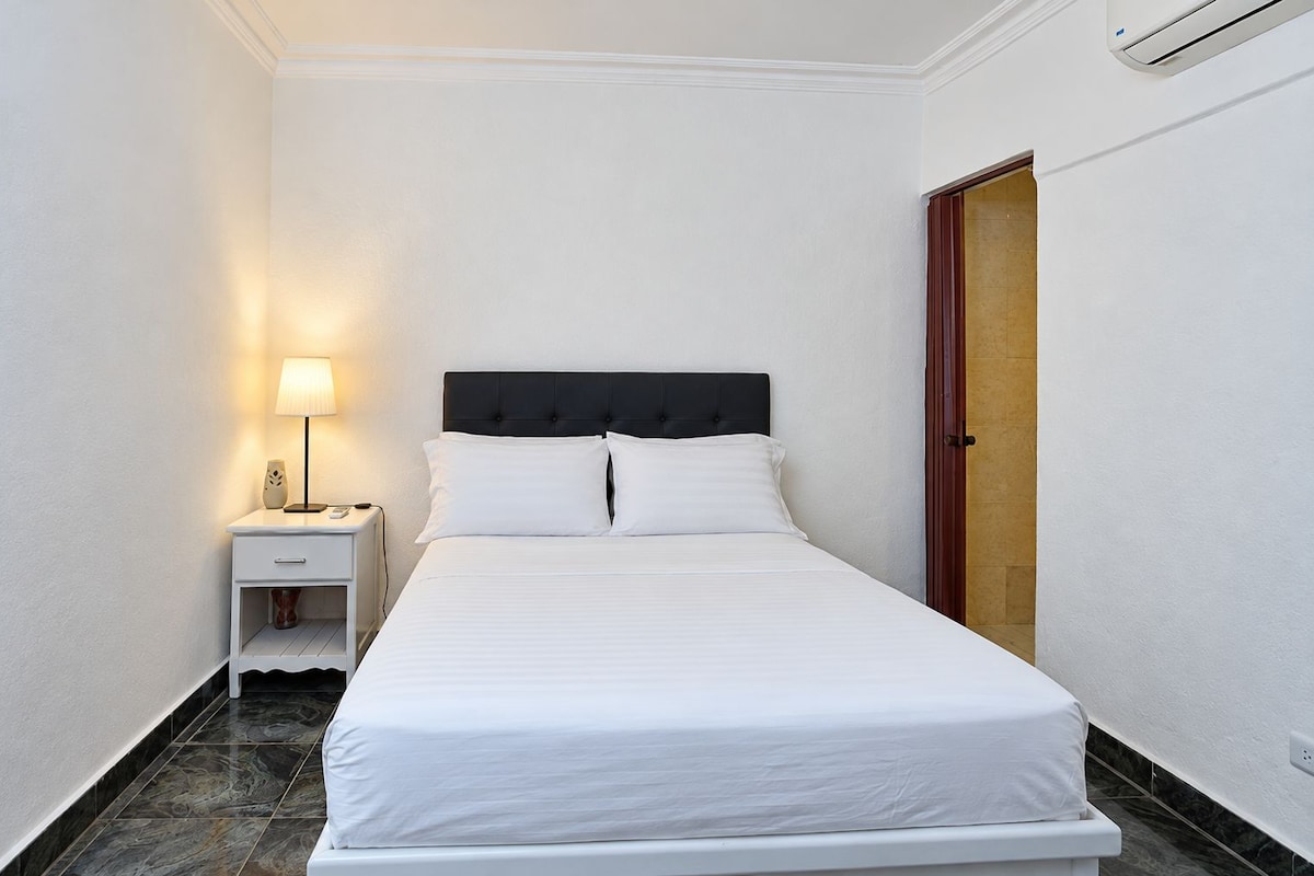 A hotel room with a bed, bedside lamp, and a door.