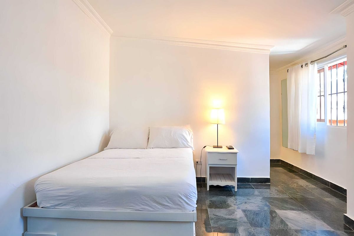 Une chambre d’hôtel avec un lit, une table de chevet, une lampe et une fenêtre avec des rideaux.
