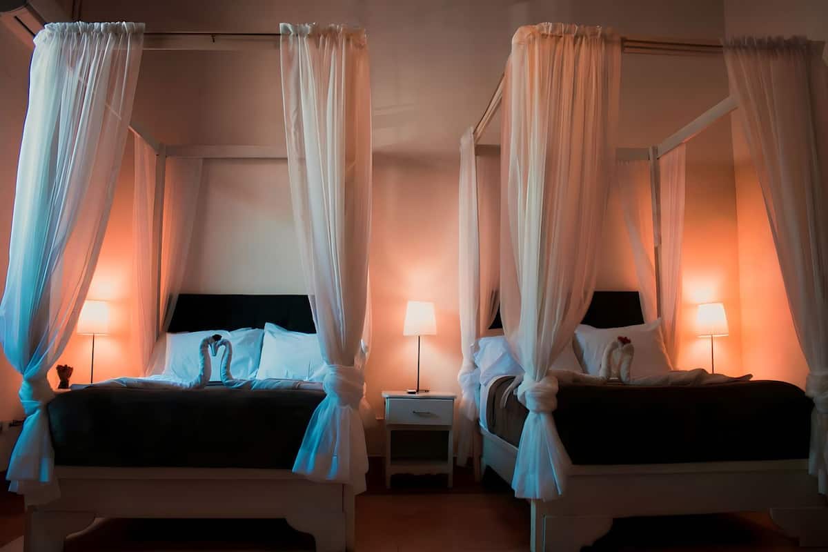 Deux lits à baldaquin blancs, des tables de chevet avec des lampes et une palette de couleurs neutres.