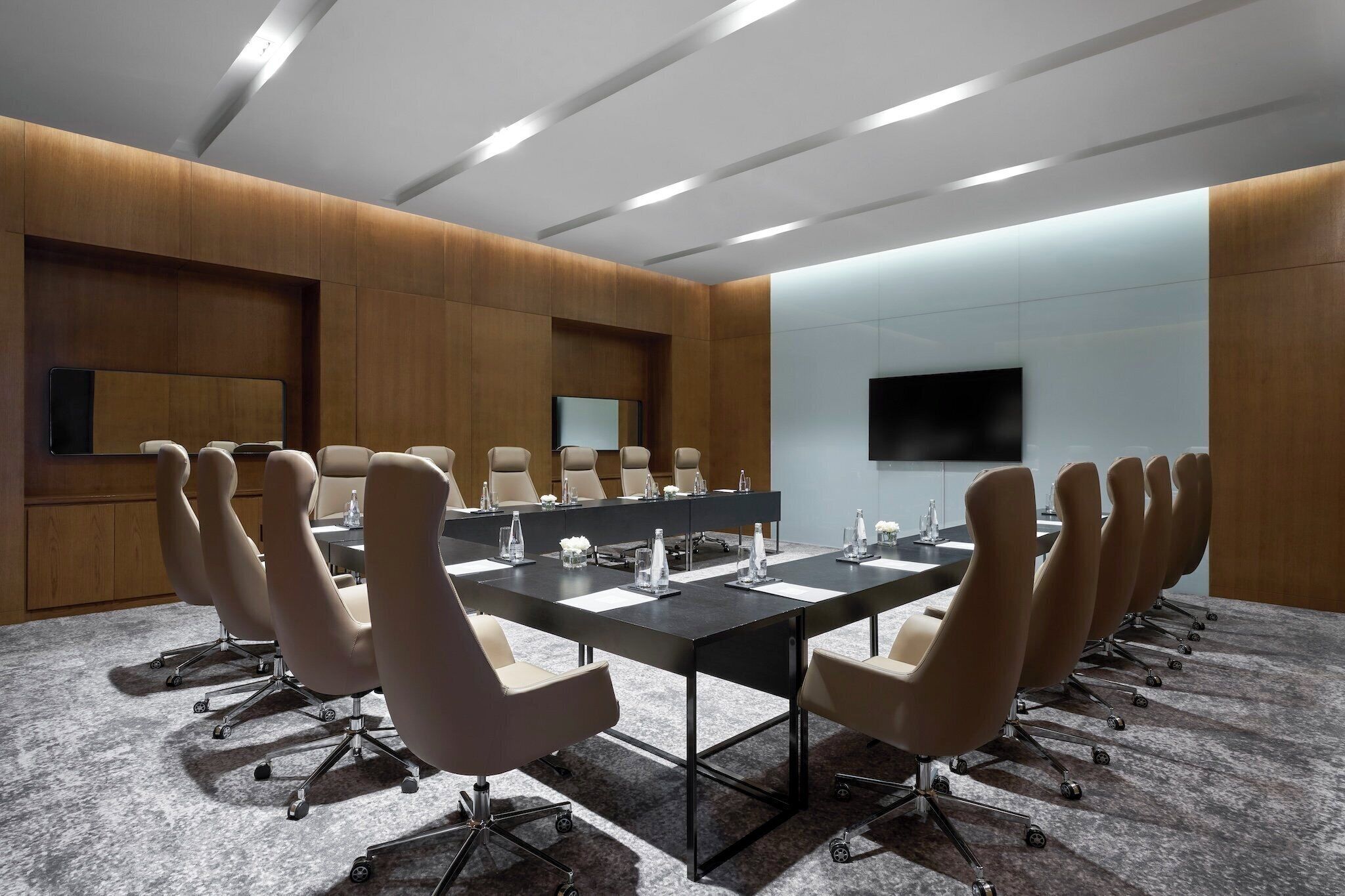 Une salle de conférence avec une longue table, de nombreuses chaises, un téléviseur à écran plat et des murs recouverts de panneaux de bois.
