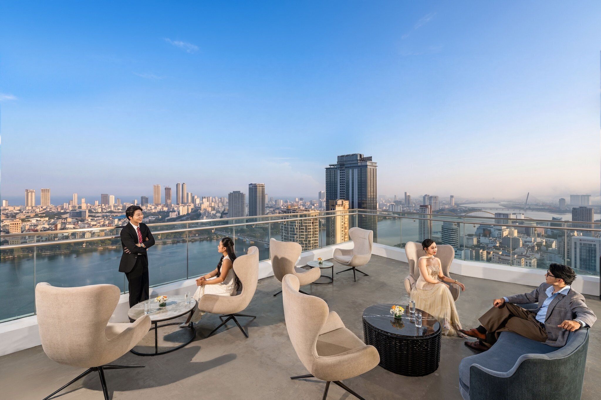 Un salón en la azotea con sillones modernos, una mesa de vidrio y vistas a la ciudad.