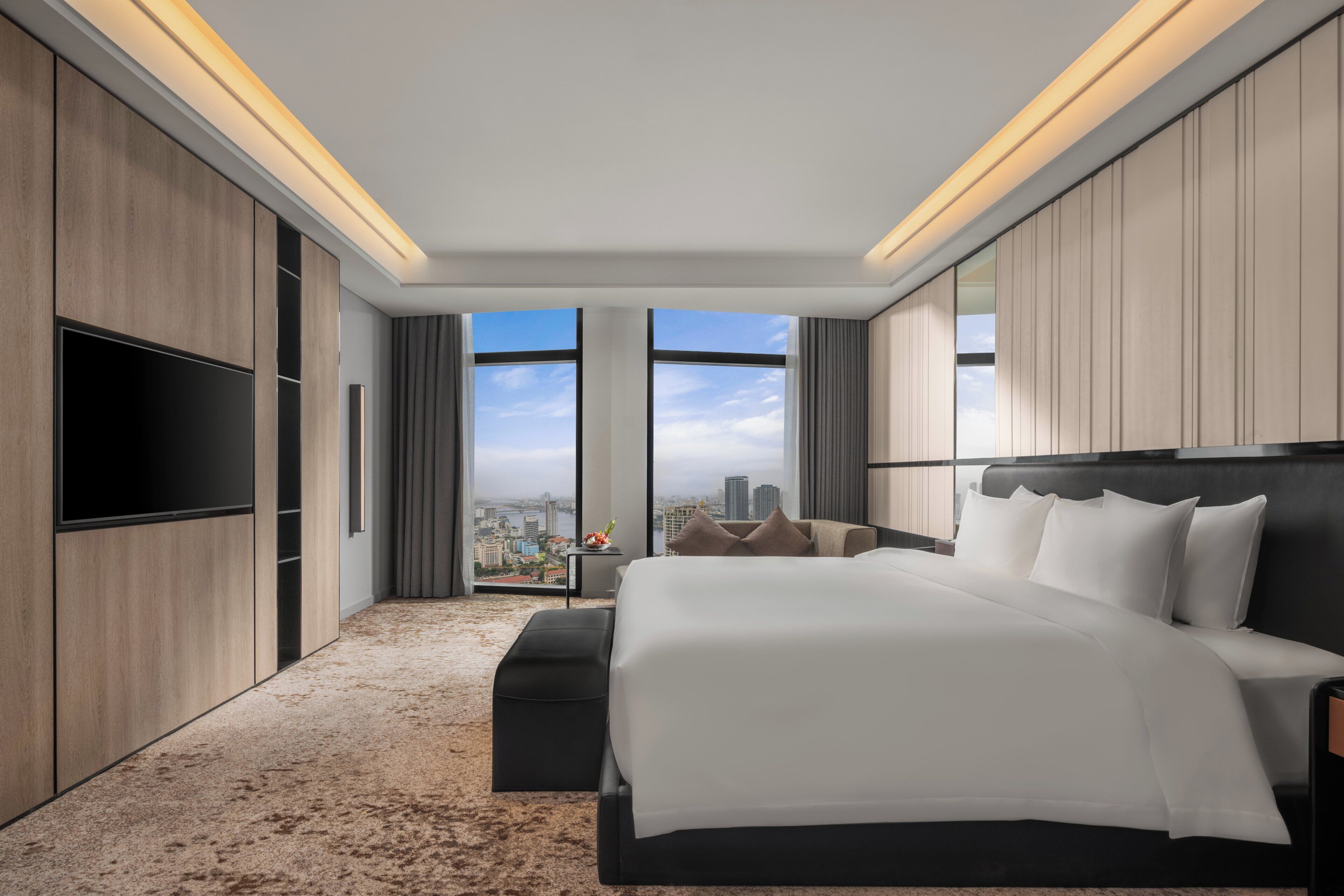 Une chambre d’hôtel moderne dotée d’un grand lit, d  ’une télévision à écran plat, d’une vue sur la ville et d’un coin salon confortable.