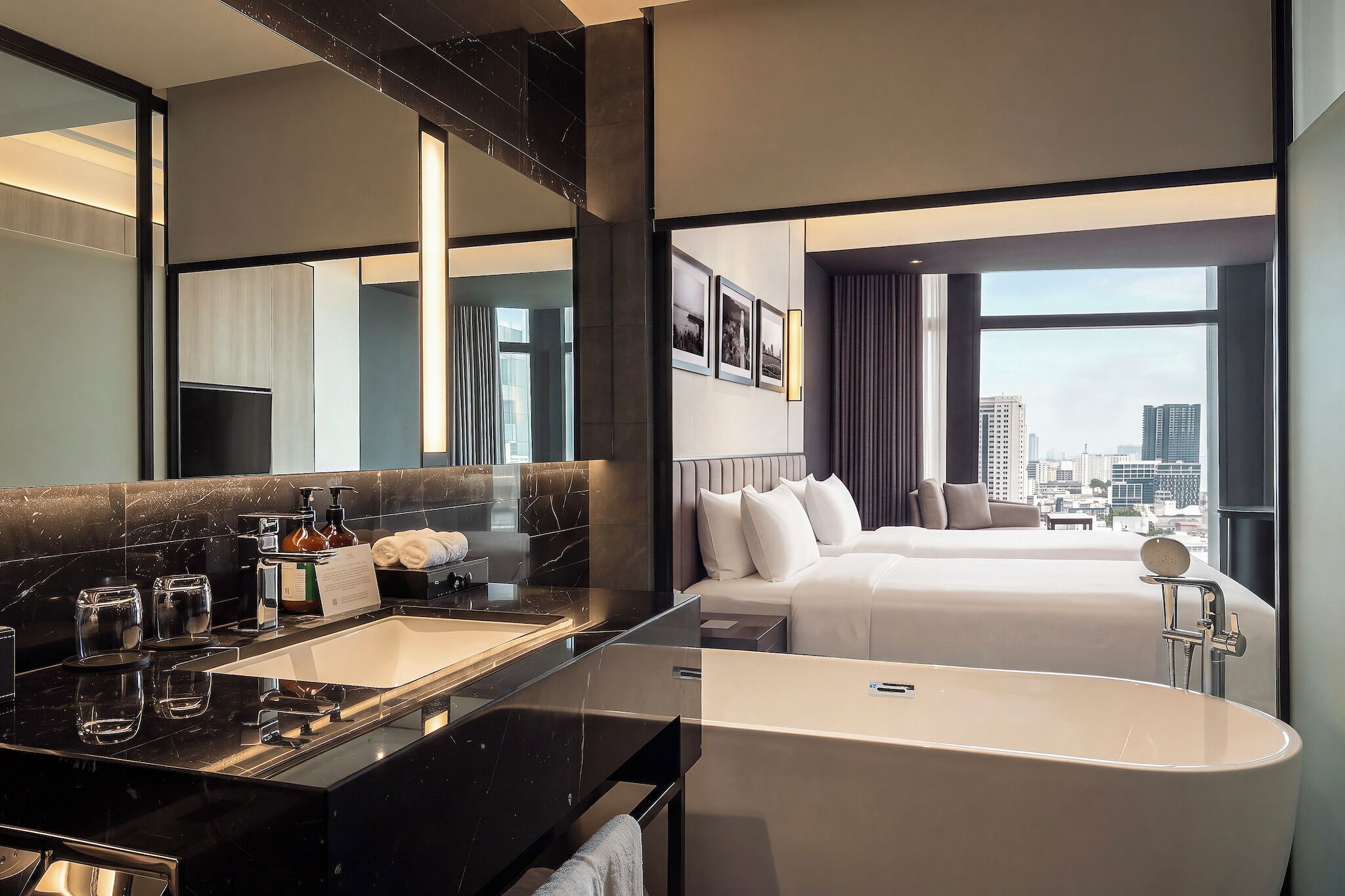 A modern hotel room with a large bed, a separate bathroom with a bathtub, a vanity with a mirror, and a city view.