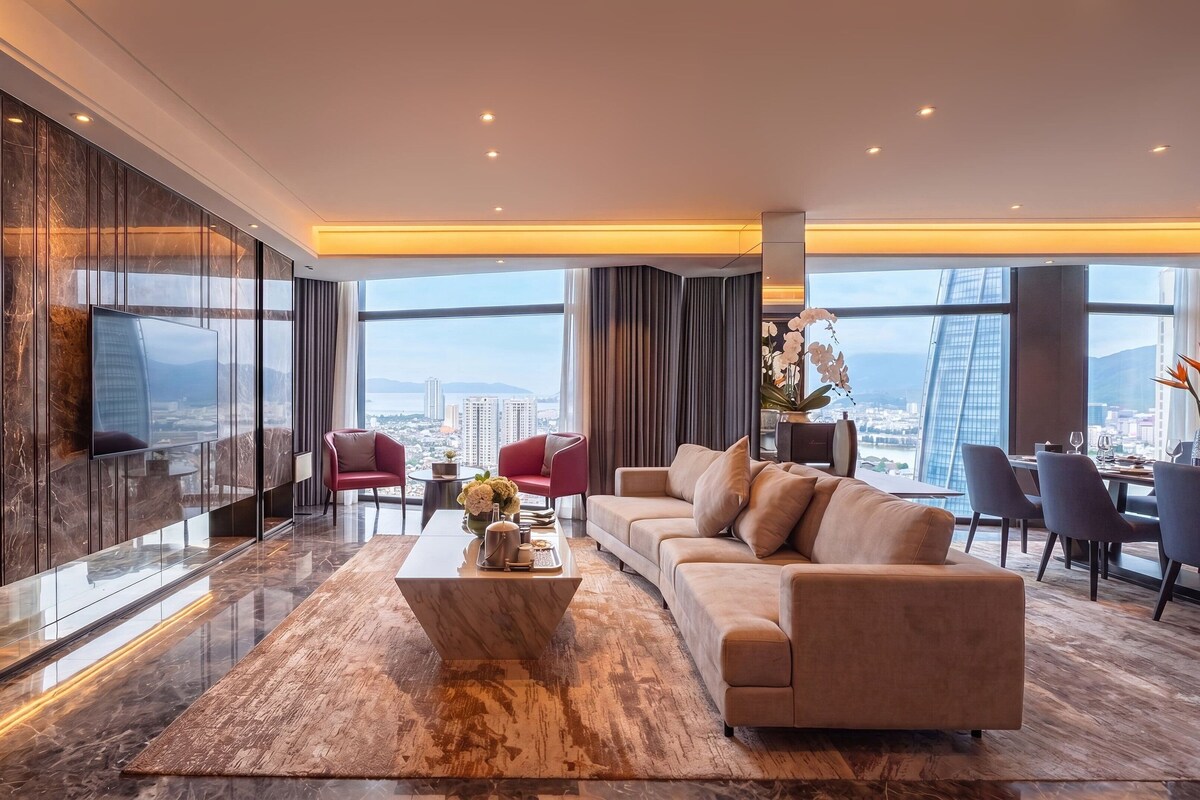A modern living room with a large sofa, a coffee table, and a TV mounted on a marble wall.
