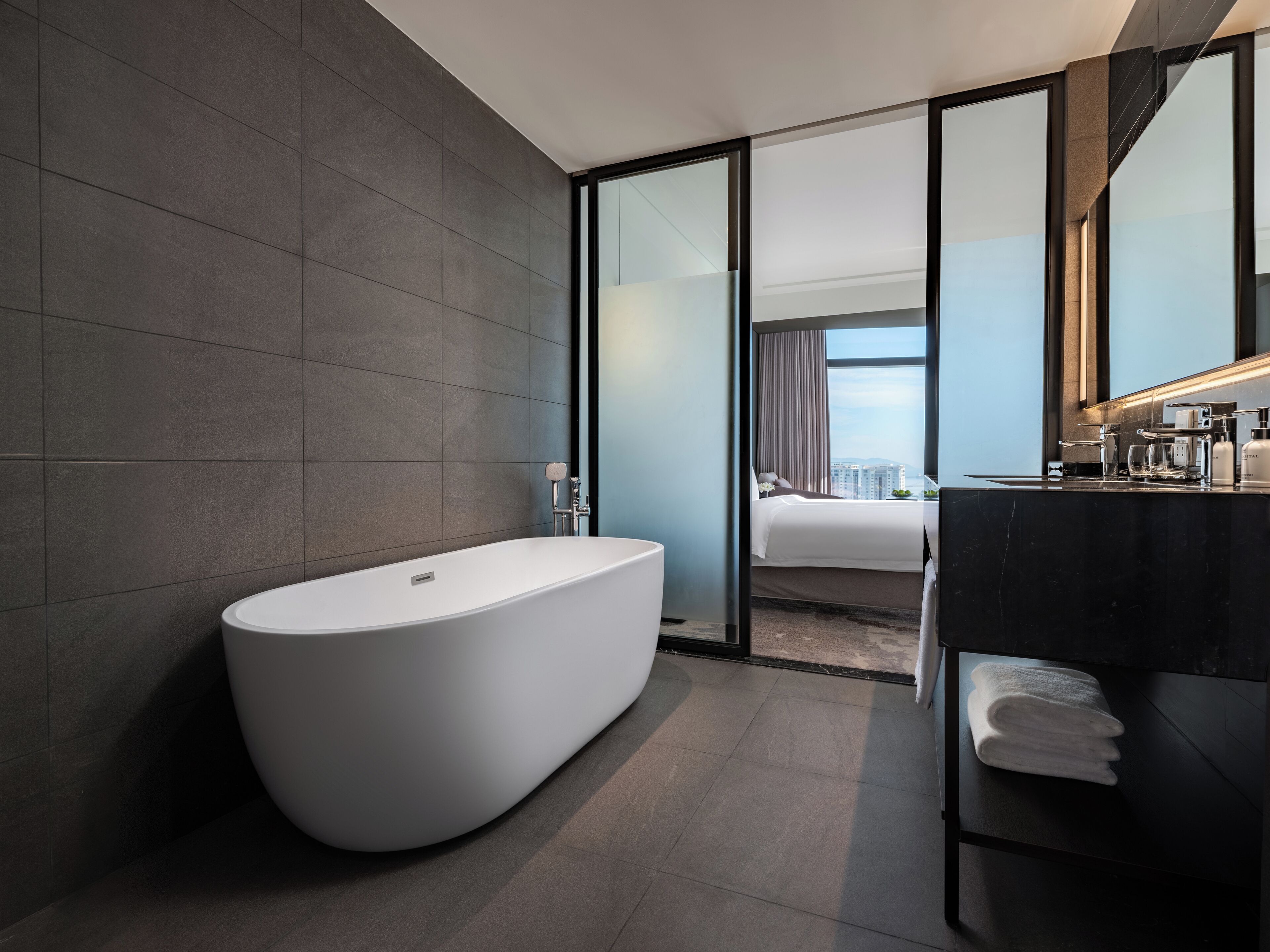 Un baño moderno con una bañera independiente, un tocador de mármol oscuro y un espejo grande.