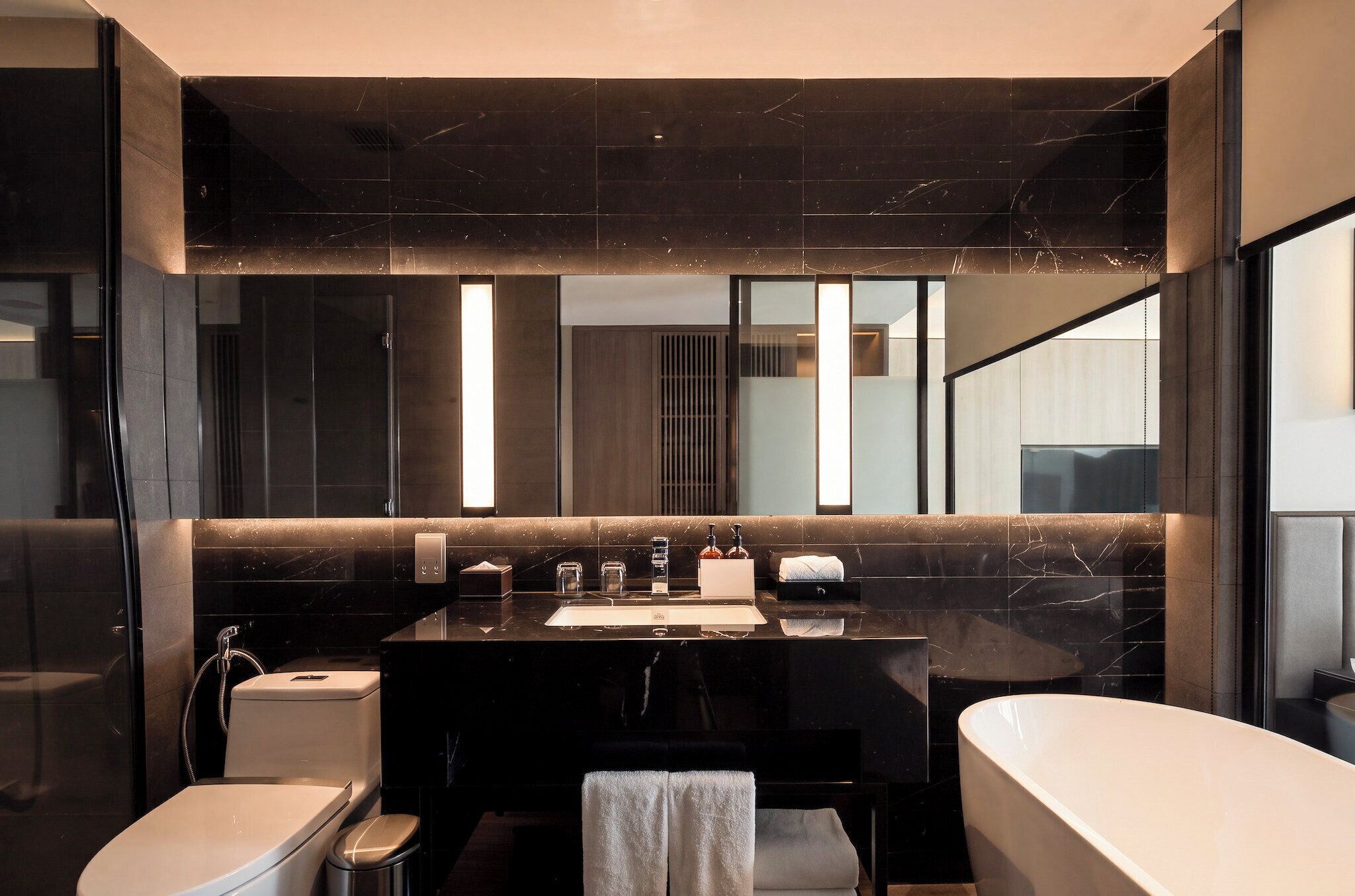 A modern bathroom with a black marble vanity, a white toilet, and a bathtub.