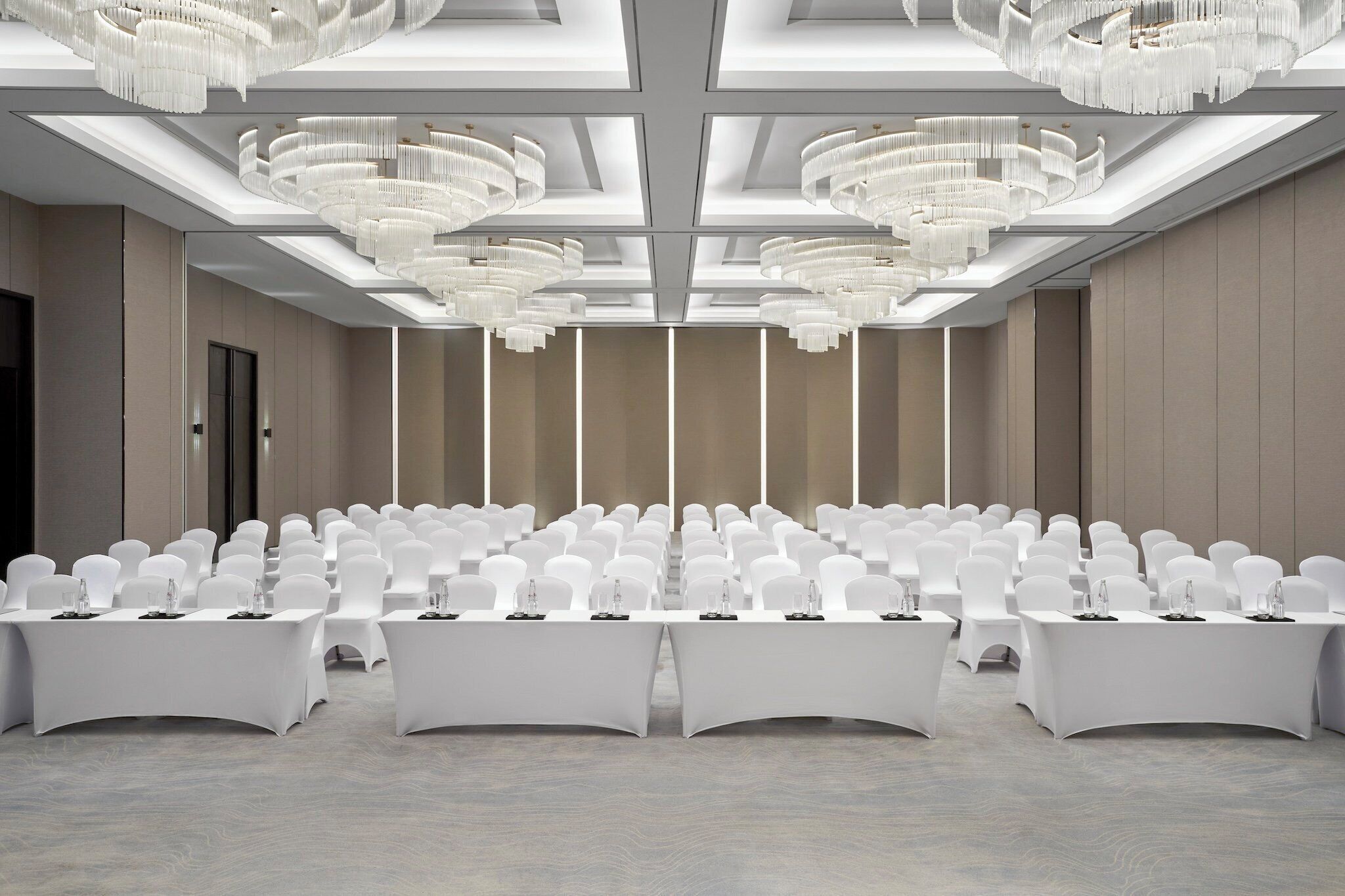Une salle de conférence avec des rangées de chaises et de tables blanches, de grands lustres et un plafond haut doté de fenêtres de toit.