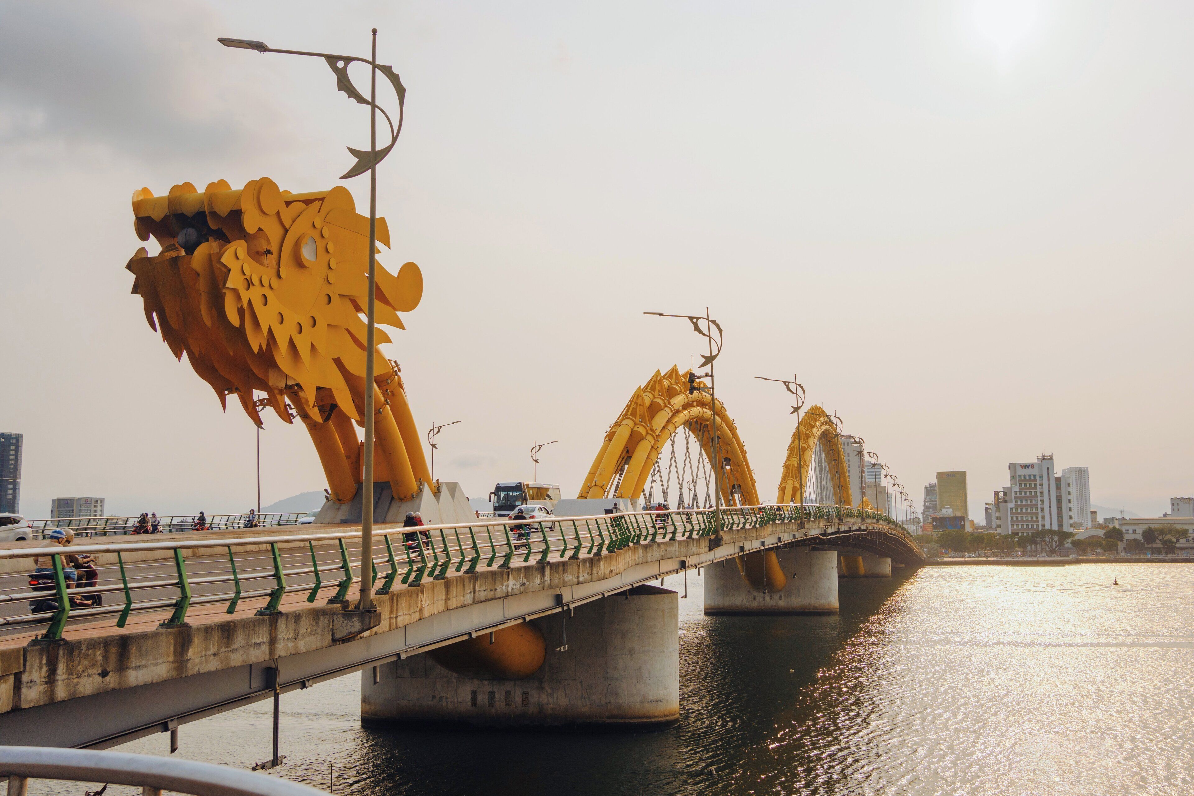 A bridge with large yellow dragon sculptures, a pedestrian walkway, and a river beneath.