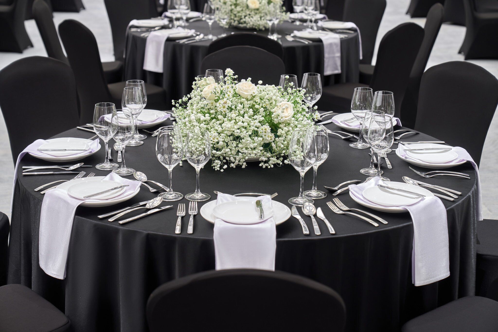 Mesa redonda dispuesta con platos blancos, cubiertos y copas de vino, con un arreglo floral en el centro.