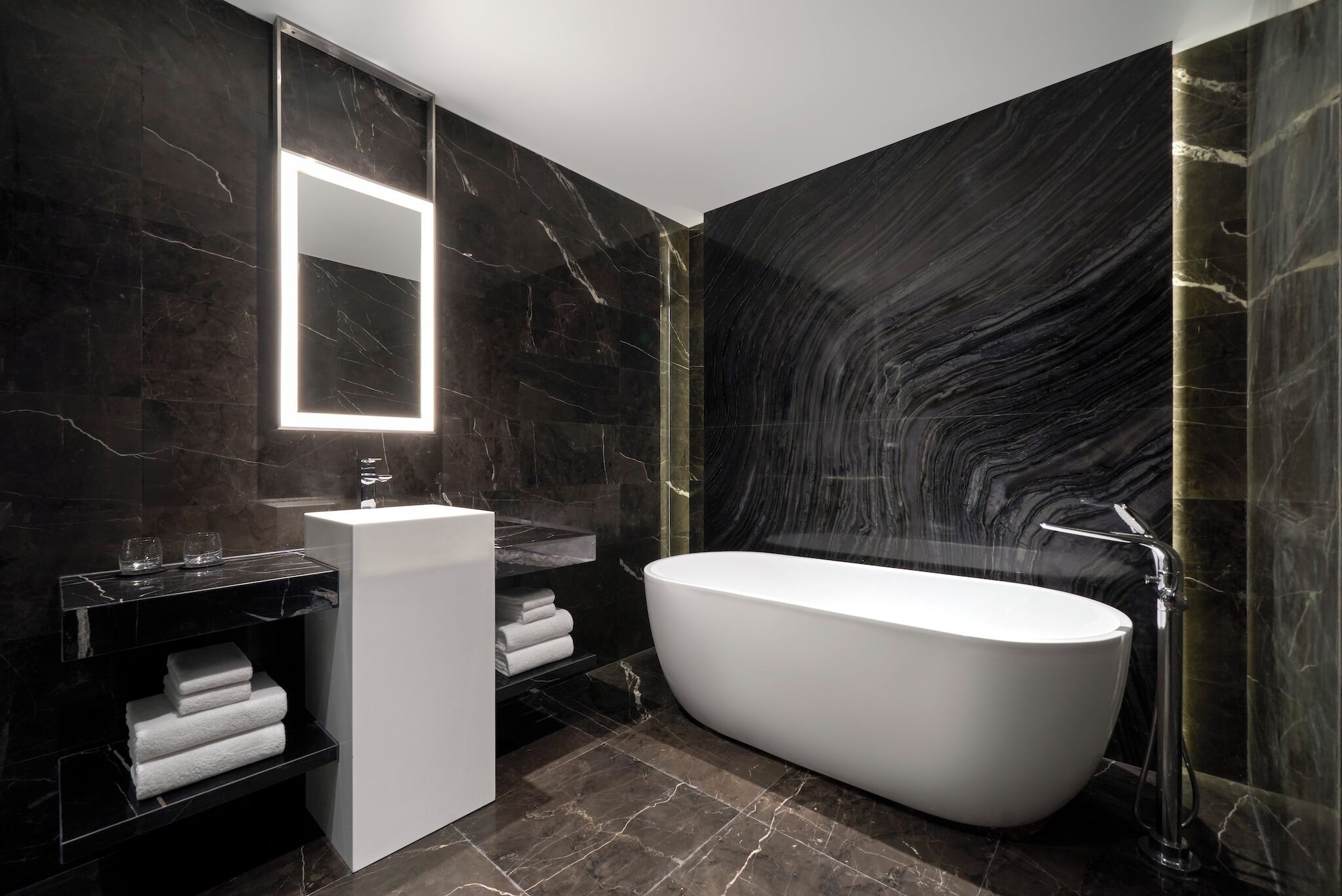 A modern bathroom with a freestanding bathtub, a large mirror, and marble walls.