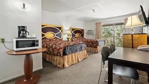 Ein Hotelzimmer mit zwei Betten, einem Esstisch, einer Mikrowelle, einer Lampe und einem Fernseher.