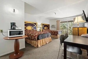 Habitación de hotel con dos camas, una mesa de comedor, microondas, lámpara y televisor.