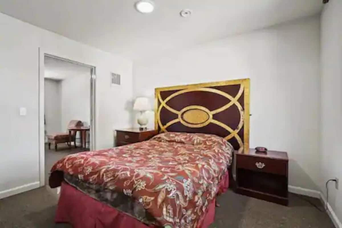 Un dormitorio con cama, mesita de noche, lámpara y silla.