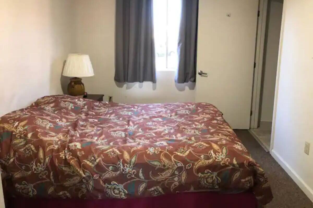 A bedroom with a bed, a nightstand, a lamp, and a window with curtains.