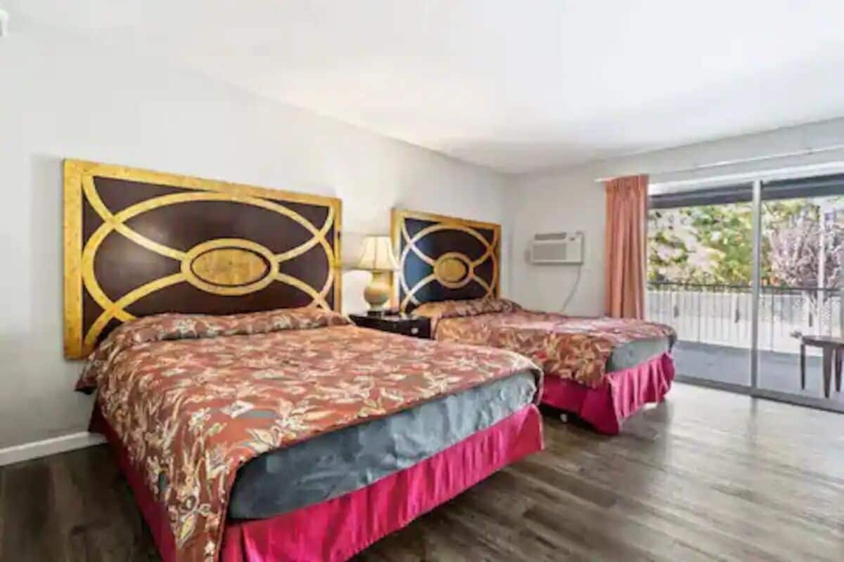 Una habitación de hotel con dos camas, un ventanal grande y un balcón.
