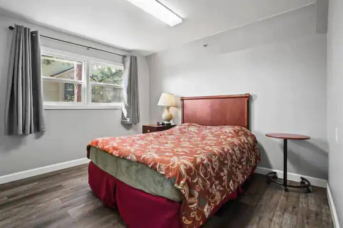 Un dormitorio con cama, mesita de noche, lámpara y una pequeña mesa.