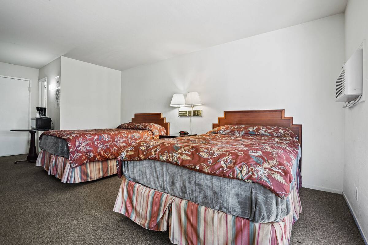 Habitación de hotel con dos camas, un escritorio, una silla, una lámpara y un equipo de aire acondicionado.