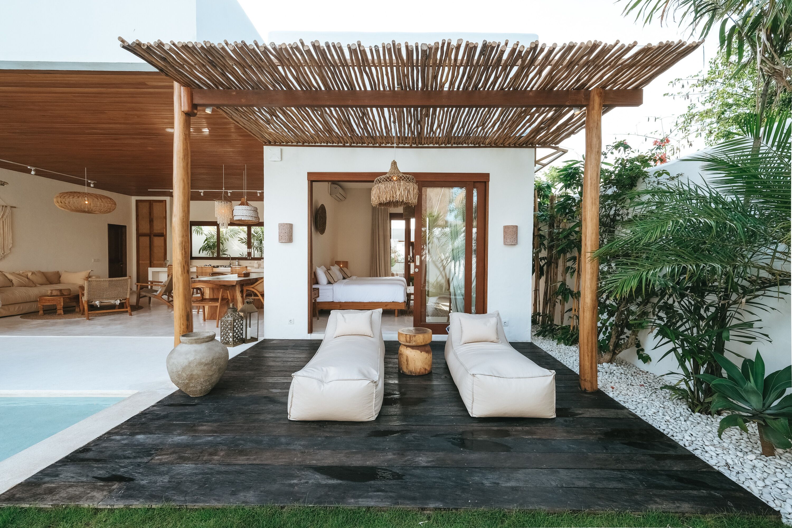 Un área de descanso exterior moderna con dos sillones color beige, una mesa de madera y una lámpara colgante.