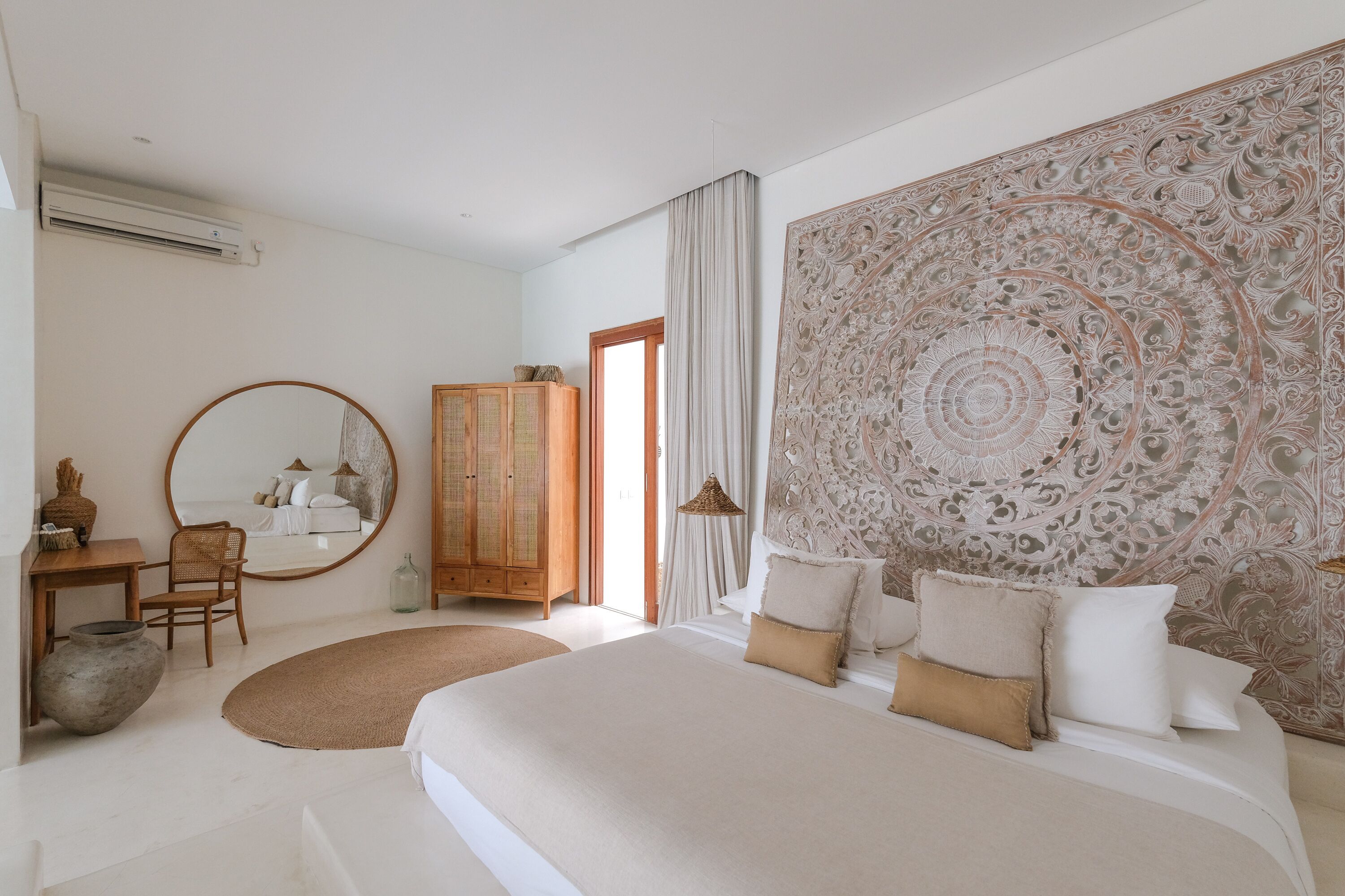 A modern bedroom with a large bed, a wooden wardrobe, a round mirror, and a decorative wall panel.