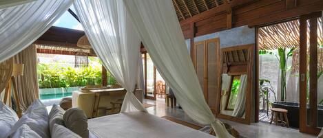 Un dormitorio con una cama grande, cortinas blancas y vistas a una zona de piscina al aire libre.