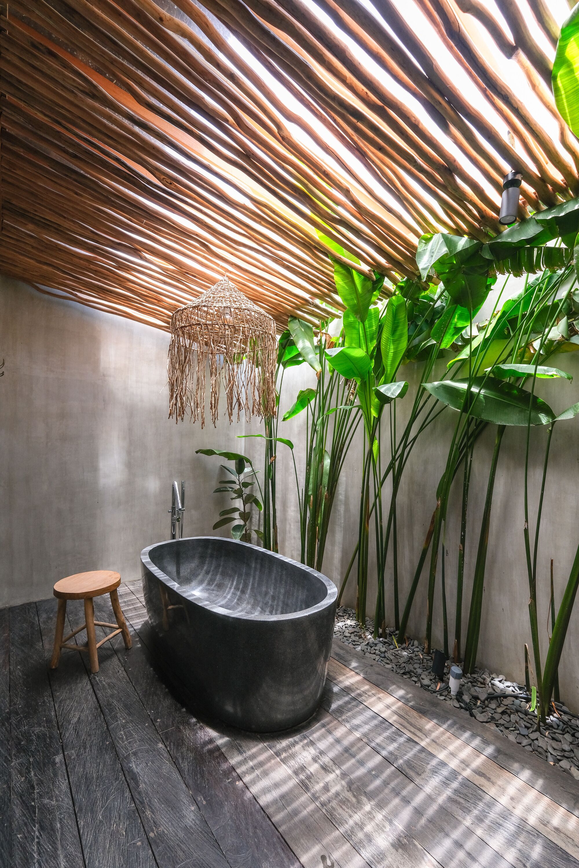 Un baño moderno con una bañera grande, un taburete de madera y plantas verdes altas.